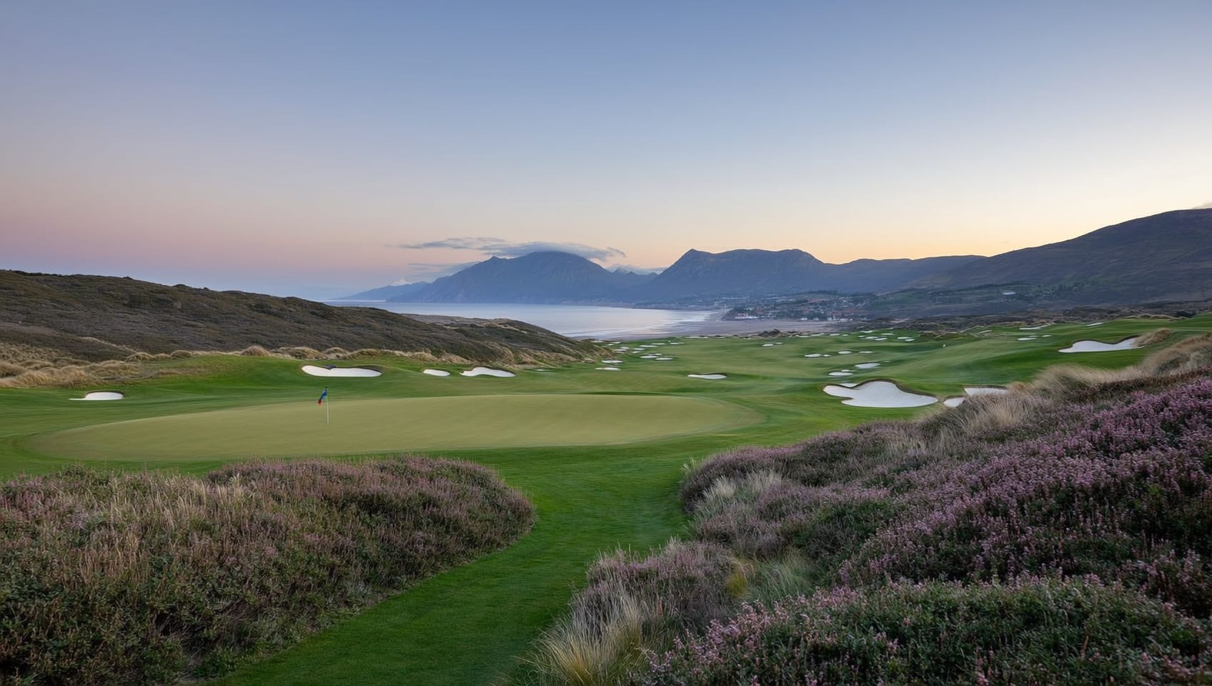 A links green at dawn with dunes and distant hills fading into golden mist, evoking the coast beneath the Mourne mountains