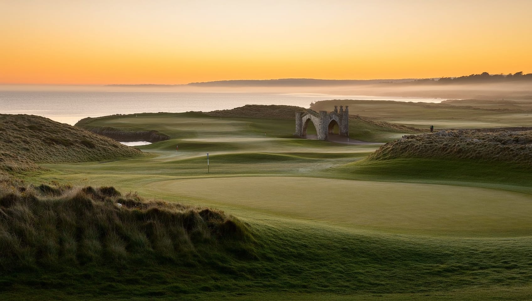 A links green at dawn with dunes and sea cliffs fading into golden mist along the coast
